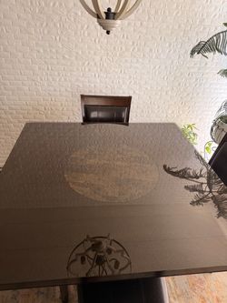 Dark glass dining table with four chairs.