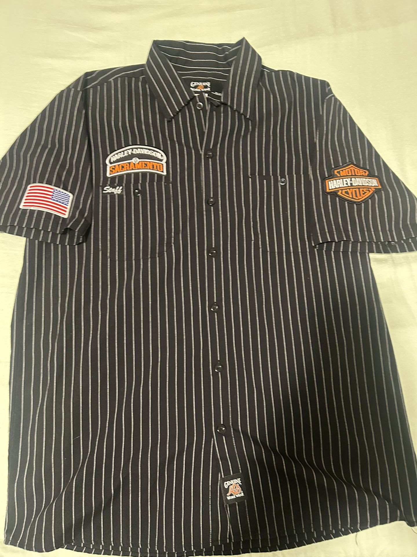 This is a Harley-Davidson men's short-sleeve button-down staff shirt with a black and white pinstripe pattern and patches .