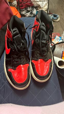 These are Nike Air Jordan 1 Retro High OG "Patent Bred" sneakers featuring a glossy patent leather finish in black and varsity red.