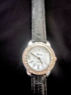 Elegant Geneva women's wristwatch has a grey textured strap. The round case is silver-toned with a gold-toned rhinestone-embellished bezel. The white