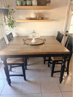 Sturdy wood dining set with a two-tone finish. The square table has a natural wood-grain top and a black-painted base with turned legs. Four matching 