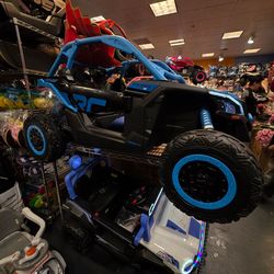 A collection of children's ride-on toys, including cars, trucks, and ATVs. The toys are made of plastic and have various features such as headlights, 