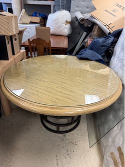 vintage glass-top dining table with a light-colored wooden frame and a dark metal circular pedestal base - 54”