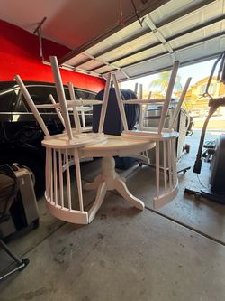 White wooden dining set includes a round pedestal table and four spindle-back chairs. The set has four dark grey fabric seat cushions. The table featu