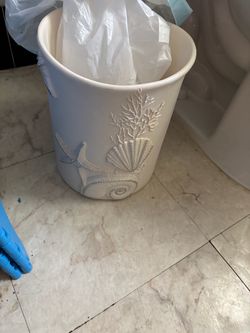 Avanti Linens Sequin Shells Wastebasket features an ivory textured resin body adorned with raised coastal motifs including a fan shell, coral, and a s