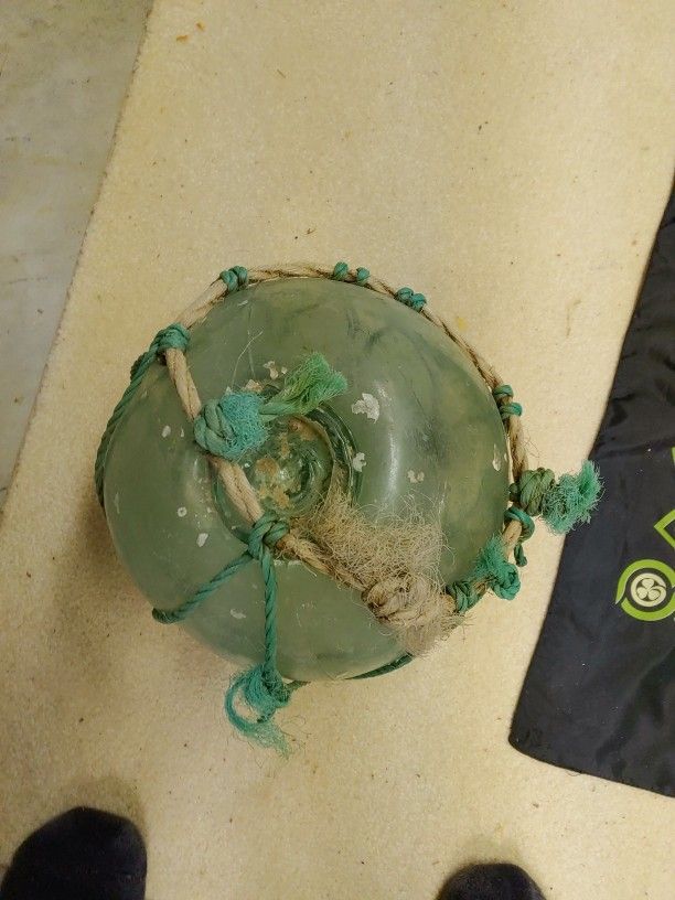 hand-blown dark green glass buoy encased in a rope Net