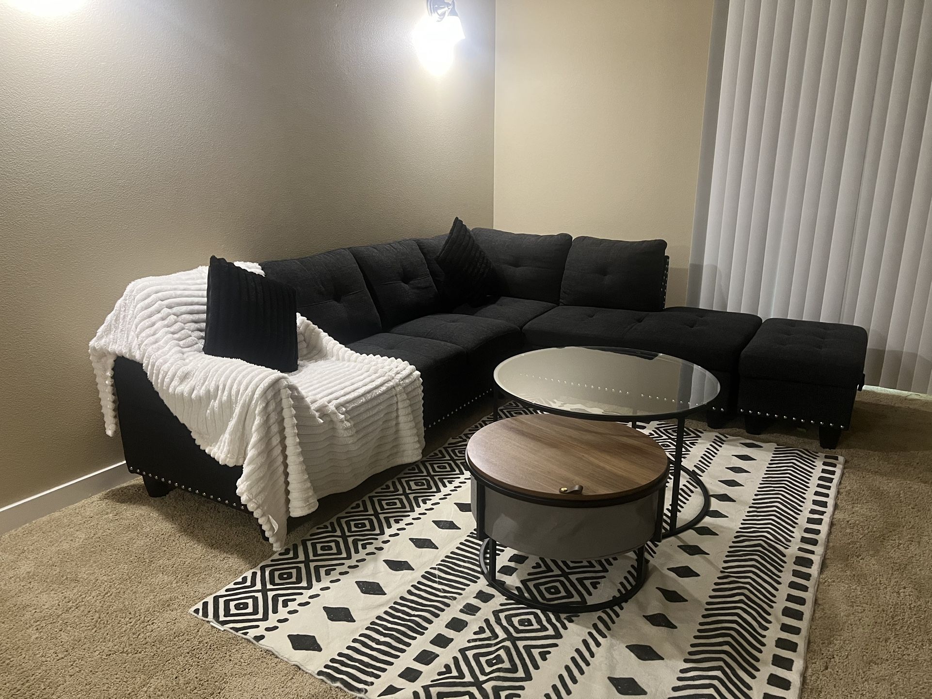 A black couch, an ottoman chair, and two tables.