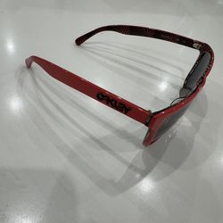Stylish red Oakley sunglasses. Has dark lenses. Temples have cool striped pattern. Model OO2035-10.