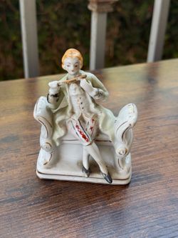 Small antique hand painted porcelain flute player sitting on a bench