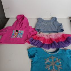 This lot of four Build-A-Bear clothes includes a hoodie, two blouses, and one two-piece skirt set. The clothing is designed for various occasions such