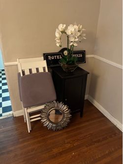 Small black ikea cabinet, 2 white folding chairs, artificial orchid, decorative mirror