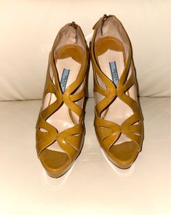 Patent leather caged heeled sandals from the luxury brand Prada. The style features crisscrossing straps with geometric cutouts, and one of the platfo