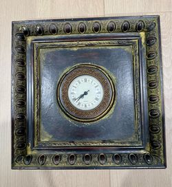 A traditional-style wall clock with a square, ornate frame