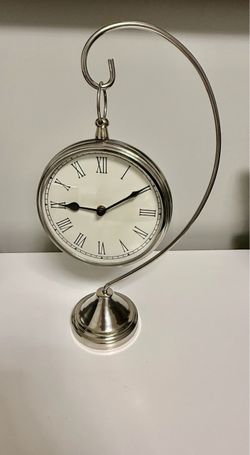 This Silver Metal Hanging Desk/Mantel Shelf Clock features a classic design with Roman numerals on its analog display, making it a stylish and functio