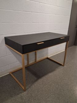 a modern black writing desk with a dark finish and gold-tone metal frame