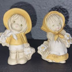 A pair of vintage UCTCI bisque ceramic figurines of children with flowers.