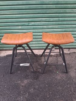 Pair of backless swivel saddle bar stool tan/cognac faux leather upholstery with vertical channel stitching, a built-in swivel mechanism, and a charco