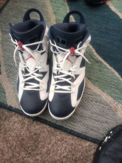 These are the Nike Air Jordan 6 Retro Olympic sneakers, featuring a white leather upper with navy blue accents and red details on the lace lock.