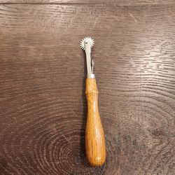 wooden-handled serrated tracing wheel features a toothed metal wheel and a contoured wooden handle with a built-in metal finger rest, good condotion