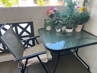 Outdoor glass face table with 4- chairs and central umbrella and feak plants .