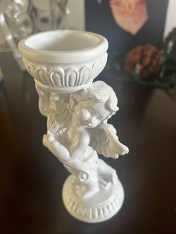 Elegant white resin candle holder with a cherub figure. This piece has a matte finish and a decorative pedestal base. The top is a fluted bowl designe