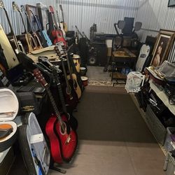 Diverse assortment of musical instruments includes multiple acoustic guitars from brands like Johnson and Jasmine, several violins in cases, clarinets