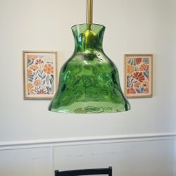 Beautiful green glass pendant light with brass fixture. The glass shade has a unique wavy pattern and is suspended from a gold cord. Good condition, n