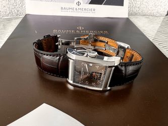 Baume & Mercier Geneve automatic watch with a rectangular stainless steel case, brown dial, Arabic numerals, small seconds subdial, and a dark brown c