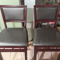 Linon Triena folding chairs featuring a rich wood finish and dark brown faux leather padding on the seat and back.  