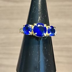 Elegant gold-tone ring featuring three vivid blue stones for a striking look. The deep blue center stone is flanked by two matching blue stones. Polis