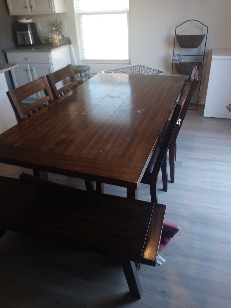 Brown table with 4 chairs and a bench.