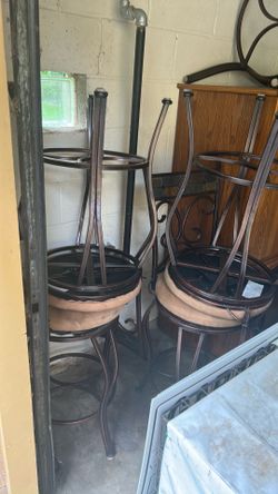 4 bar chairs with backs, one glass table , and wooden chest .