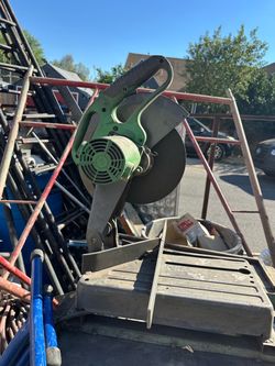 Heavy-duty metal cut-off saw has a 14-inch wheel capacity and a 15A, 1750W motor. This Hitachi CC 14SF model is green and grey with a metal base and a