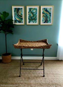 Anthropologie Maude Rattan Tray Table features a natural woven wicker tray on a foldable iron base. 22"×15"×21"