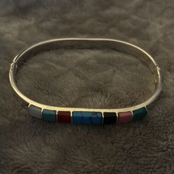 vintage Taxco sterling silver hinged bangle bracelet featuring inlaid multi-colored stones, often including turquoise, coral, and onyx.