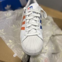 Adidas Superstar J' model with the colorway Cloud White/Blue/Gold Metallic