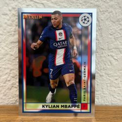 Kylian Mbappé trading card featuring PSG kit. Bold navy blue jersey with red and white vertical stripe. Clear player name and team text. Glossy collec