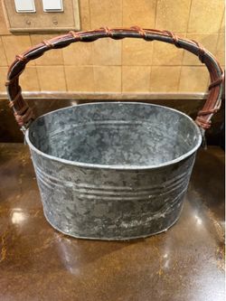 Galvanized metal oval bucket that features a rustic style with a woven swing handle