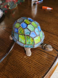 Tiffany-style lamp features a handcrafted stained glass shell in shades of blue and green, set on a cast metal base.