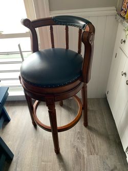 item is a traditional swivel wooden bar and counter stool featuring a dark blue/grey leather-upholstered round seat and low curved backrest, brass nai