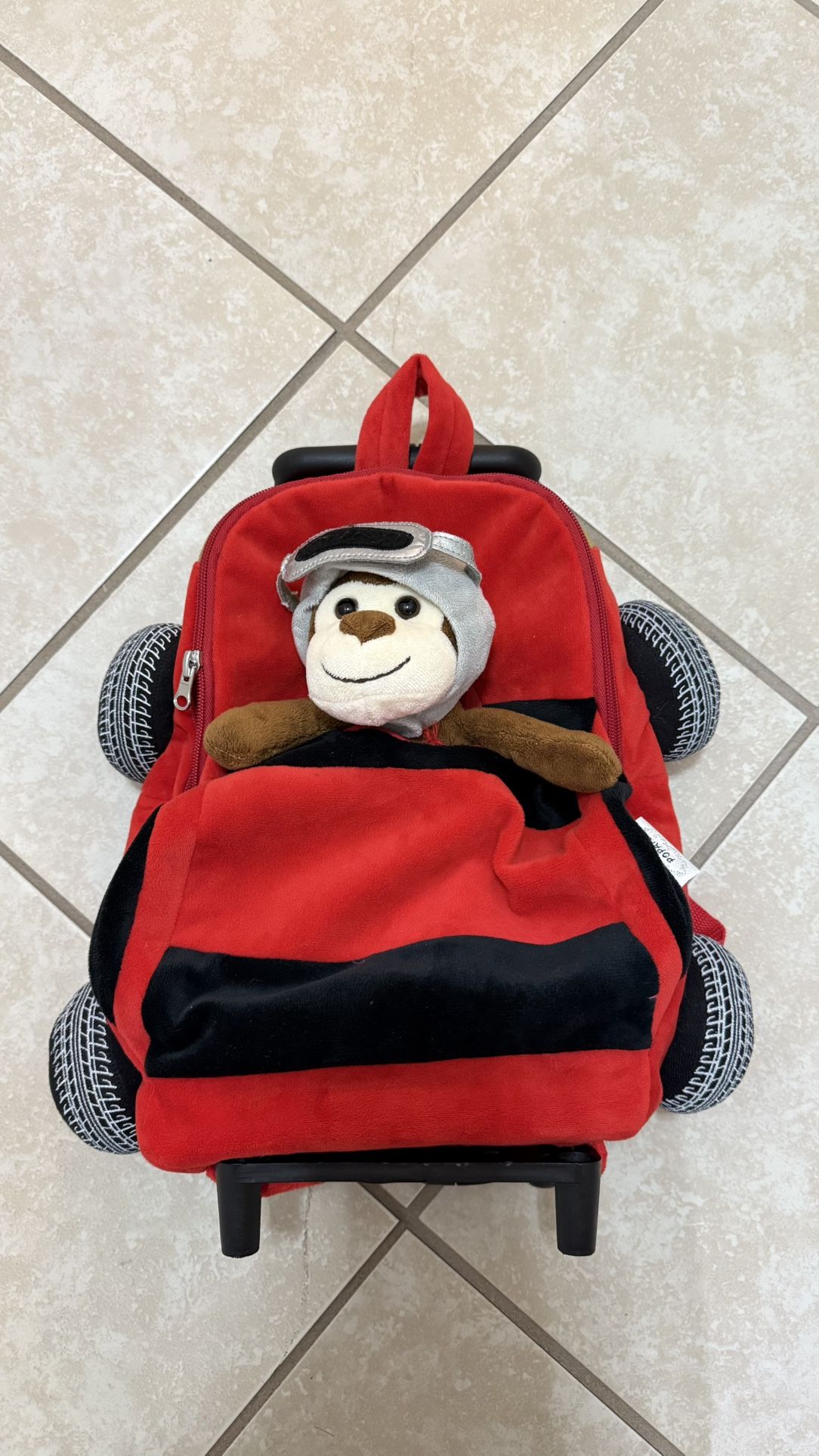 Red car luggage with attached monkey toy and wheel design.