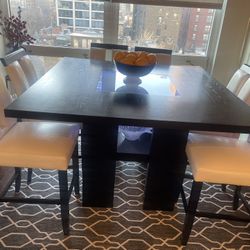 Elegant and sophisticated 54”x54” square dining table with glass centerpiece inlay, six white chairs with faux white leather and black accents. Extrem