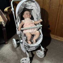 A toy stroller for dolls—specifically the convertible model from Pottery Barn Kids—with a baby doll included.color gray