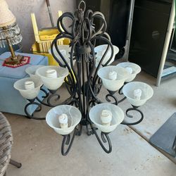 This is a black metal 10 light chandelier featuring curved scrollwork and frosted glass shade