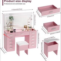 Pink vanity set constructed from wood and glass. This set includes a large rectangular mirror, a desk with nine drawers, and a matching storage stool 