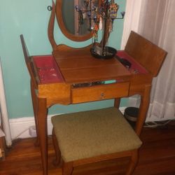 Queen Anne style wooden vanity set with an oval mirror and cushioned stool. 