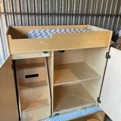 Jonti-Craft changing table with remote control. Made of wood, it features pull-out steps with child-safe surfaces and built-in storage.