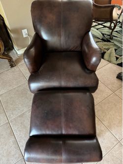 Brown leather armchair with a matching ottoman and decorative nailhead trim.