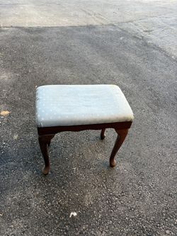 Vintage stool. Wooden, with curved legs. Seat upholstered in light blue fabric with a subtle geometric pattern.