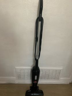 Lightweight Bissell Featherweight stick vacuum is black with a silver handle. This corded vacuum has a bagless design and a removable floor nozzle.